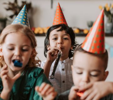 Gruppe feiernder Kinder mit Partyhut und Tröte.